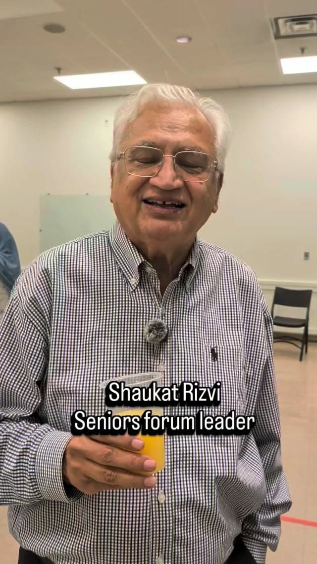 Shaukat Rizvi, seniors forum leader, smiling in a community hall while recording a message of support for Zena
